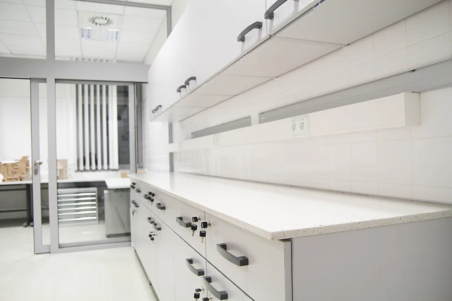 Długi ciąg stołów laboratoryjnych z szafkami, szufladami i listwą techniczną.