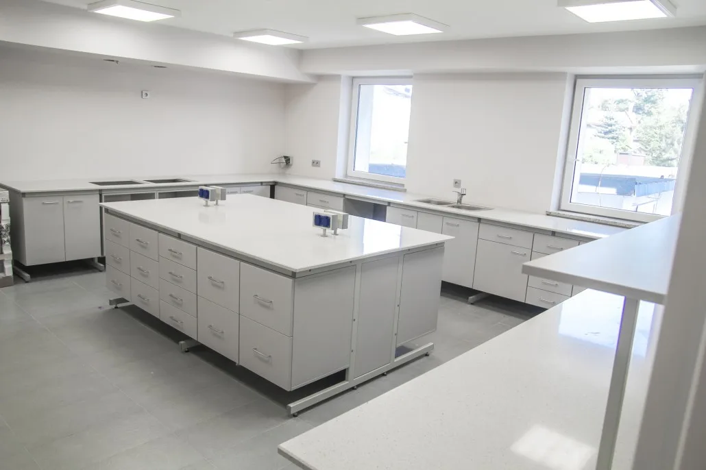 Małe laboratorium przemysłowe z wyspą roboczą, zlewami i szafkami.