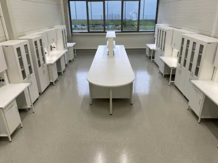 Pracownia laboratoryjna z wyspą roboczą, szafkami i stanowiskami przyściennymi.